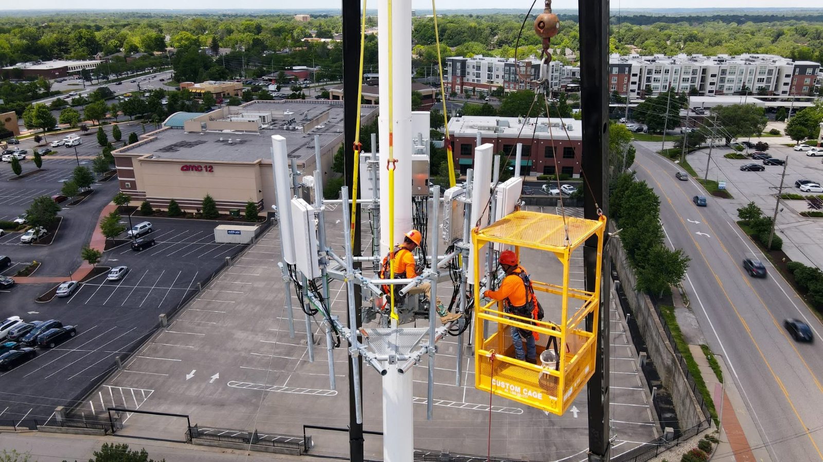 The client's own aerial drone photograph: two workers in orange high-visibility gear on the platforms of a communications